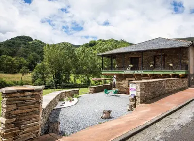 a building with a stone wall and a patio at Albergue El Paso in Vega de Valcarce
