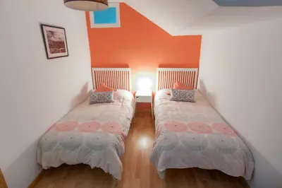 two beds in a room with an orange wall at Entrepexigos in Santiago de Compostela