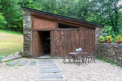 a table and chairs in front of a wooden shed at Casas del Molino - Muiños do Mainzoso Turismo Rural in Paderne