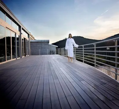 a woman in a white robe standing on a wooden deck at ARNOIA CALDARIA HOTEL Y BALNEARIO in Arnoia
