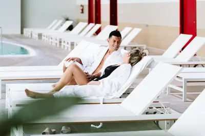 a man and woman sitting on lounge chairs next to a pool at Laias Caldaria hotel y Balneario in Laias