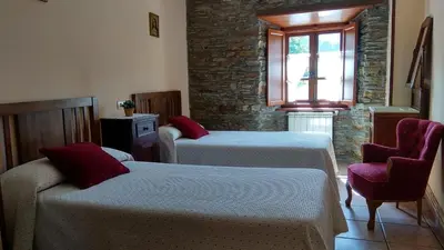 a bedroom with two beds and a chair and a window at Apartamentos Los Castros in San Tirso de Abres