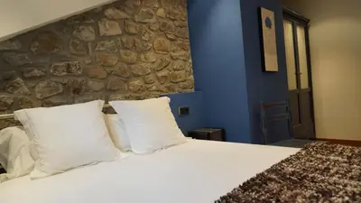 a bedroom with a white bed with a stone wall at Apartamentos Lagos de Saliencia in Saliencia