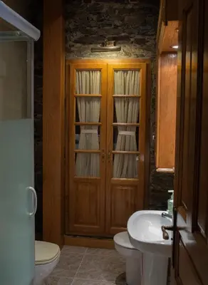 a bathroom with a toilet sink and a wooden door at Apartamentos Rurales Las Mestas in Puenteciella