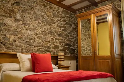 a bedroom with a stone wall and a bed with a red pillow at Apartamentos Rurales Las Mestas in Puenteciella