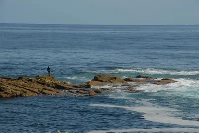 a person standing on a rock in the ocean at Hotel Playa de las Catedrales in Reinante