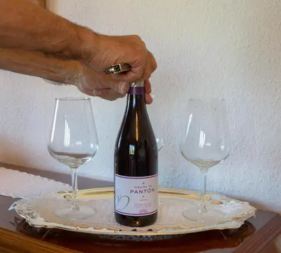 a person opening a bottle of wine next to two wine glasses at Villa con piscina en Pantòn Ribeira Sacra Galicia Ideal para familias in Pantón