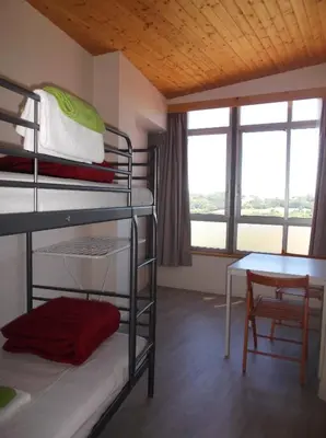 a room with bunk beds and a table and window at O Cabalo Verde in Palas de Rei