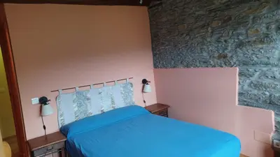 a bedroom with a blue bed and a stone wall at A Palleira in Castro Caldelas