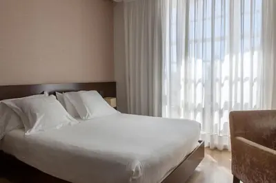 a bedroom with a bed with white sheets and a window at Hotel San Miguel in Santiago de Compostela