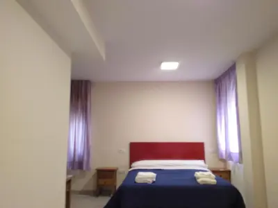 a bedroom with a bed with blue sheets and purple curtains at Hostal Orly in Camponaraya