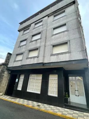 a gray building with white windows on a street at Hotel Victorino in Silleda