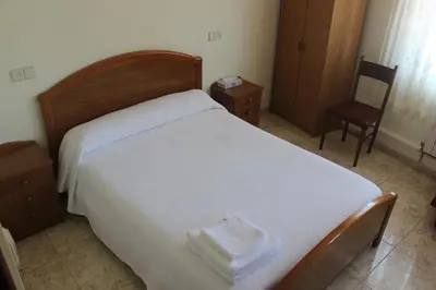 a bedroom with a white bed with a wooden frame and a chair at O Cruceiro in Puentedeume