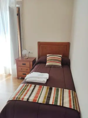 a bed with a striped blanket and a night stand at Pension a Fontiña in Cuntis
