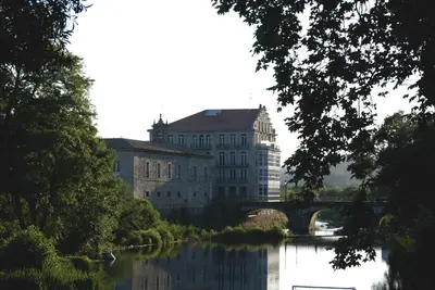 a large building next to a river with a bridge at Balneario Acuña in Caldas de Reis