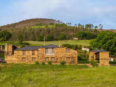 a stone house in a field with a hill in the background at Complejo Rural Lar de Vies in A Pontenova