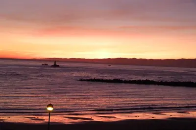 a sunset over the ocean with a light on the beach at Hotel Nordés in Burela de Cabo