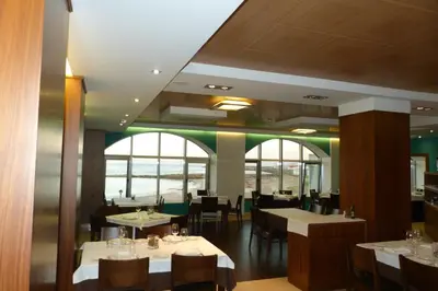 a dining room with tables and chairs and windows at Hotel Nordés in Burela de Cabo
