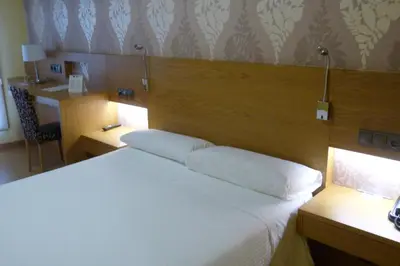 a bedroom with a white bed and a desk with a chair at Hotel Nordés in Burela de Cabo