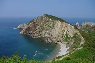 a large rocky mountain with a beach and the ocean at Hotel Rural Suquin in Navia