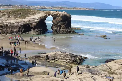 a group of people on a beach near an arch in the ocean at Costa Reinante Spa in Barreiros