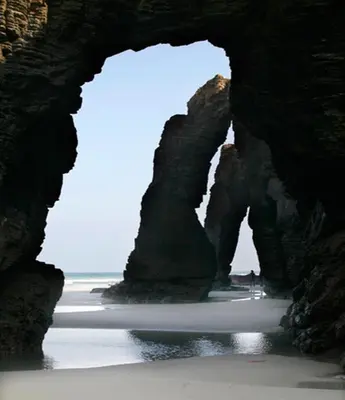 a cave on a beach with the ocean behind it at Costa Reinante Spa in Barreiros
