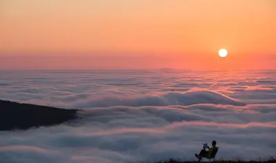 a couple sitting on a hilltop above the clouds at sunset at A Casoa II in Santa Eulalia de Oscos