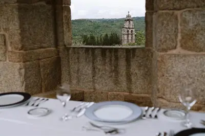 a table with plates and glasses and a view of a tower at Casa Rural Rectoral de Armariz in Nogueira de Ramuin