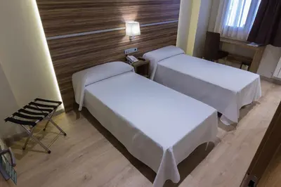 a hotel room with two beds and a chair at Hotel Novo Cándido in Ourense