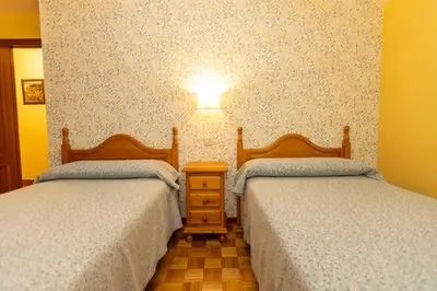 a bedroom with two beds and a light on the wall at Escuder Apartamentos Turísticos in Ribadeo