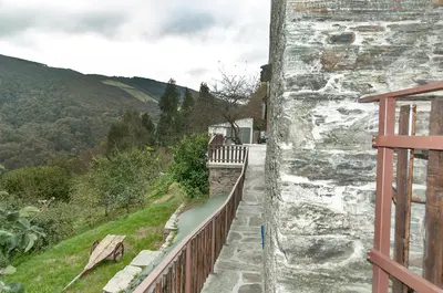 a stone building with a wooden fence next to a road at Apartamentos Casa Ramoncín in A Pontenova