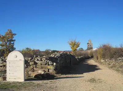 a tombstone next to a stone wall with a clock tower at Via Avis in Santa Catalina de Somoza