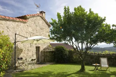 a garden with an umbrella and a table and a tree at Casa de Afora Casa con piscina y jacuzzi privados in Santiago de Compostela