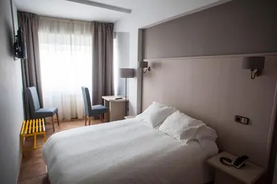 a hotel room with a bed and two chairs and a window at Hotel Brial in Perillo