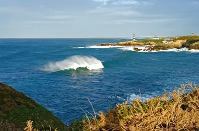 a wave in the ocean with a lighthouse in the background at Finca Goleta in Foz