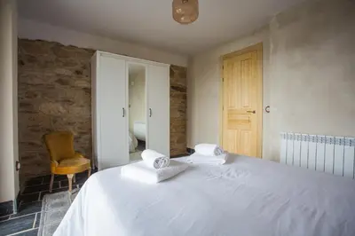 a bedroom with a white bed with a yellow chair at Os Feleitos in Orellán