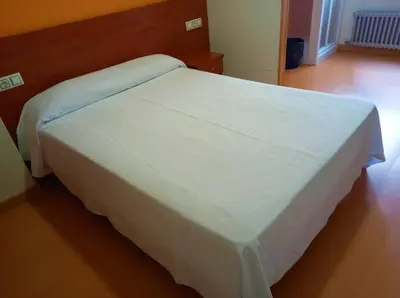 a white bed in a bedroom with a wooden floor at Pension San Roque in Lugo