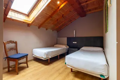 two beds in a room with a chair and a window at PENSION CASA MIÑO in Pola de Somiedo