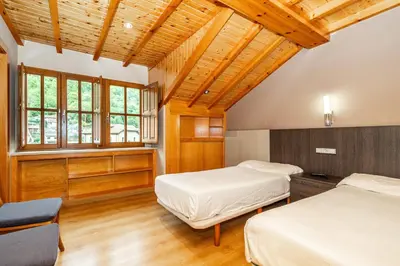 two beds in a room with wooden ceilings and windows at PENSION CASA MIÑO in Pola de Somiedo