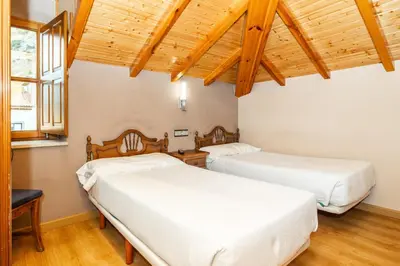 two beds in a room with wooden ceilings at PENSION CASA MIÑO in Pola de Somiedo