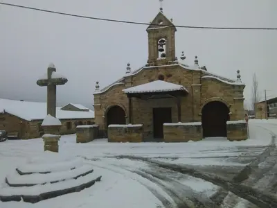 a stone church with a cross in the snow at Hotel Rural Molino del Arriero in Luyego de Somoza