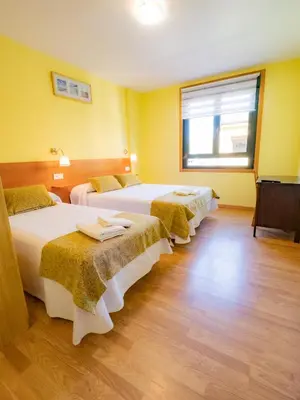 three beds in a room with yellow walls at Pensión Palas in Palas de Rei