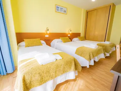 a room with three beds with yellow walls and wooden floors at Pensión Palas in Palas de Rei