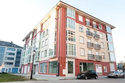 a red and white building with a car parked in front at Pensión Rúa Peregrino in Sarria