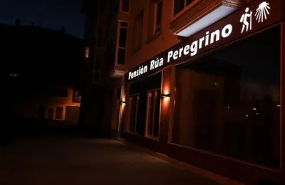 a sign on the side of a building at night at Pensión Rúa Peregrino in Sarria