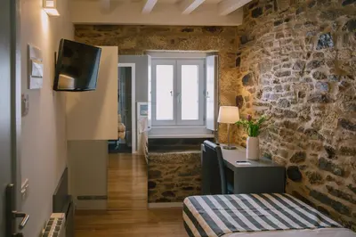 a room with a stone wall with a bed and a tv at Os Sobriños Do Pai in Santiago de Compostela