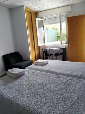 a room with two beds and a chair and a window at O Cruceiro in Palas de Rei
