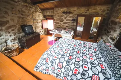 a bedroom with a large bed and a stone wall at Caserío da Castiñeira in Sas do Monte