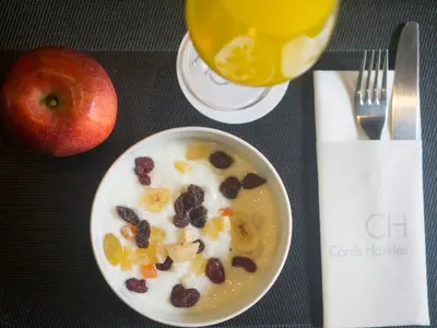 a bowl of cereal with raisins and an apple and a drink at Carris Cardenal Quevedo in Ourense