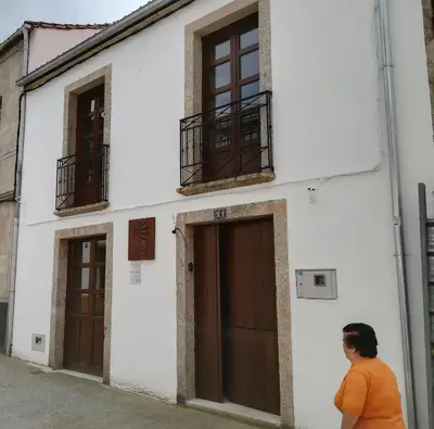 a woman walking in front of a white building at Albergue O Candil in Melide